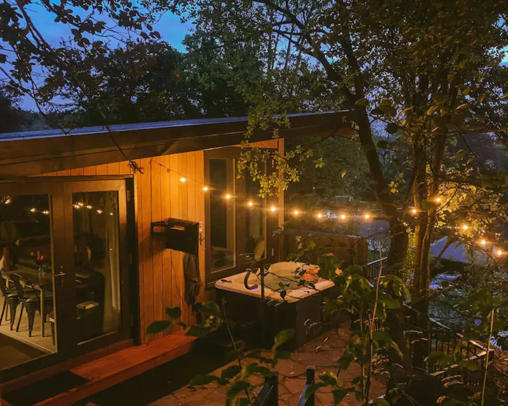 An exterior view of The Bird's Nest romantic stay in New Zealand with hot tub and festoon lights outside