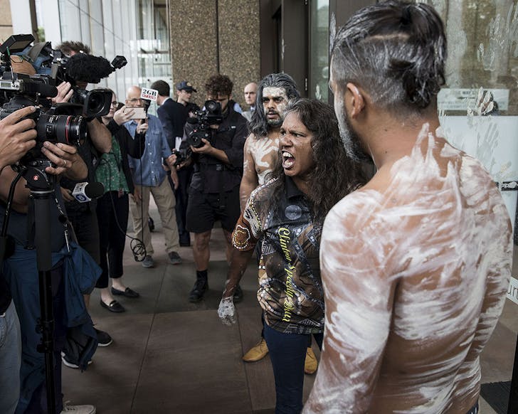 Three Aboriginal people protest outside high court while cameras cluster around.