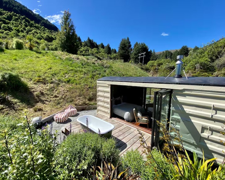 An exterior view of the green Box Car romantic stay near Queenstown, New Zealand, with outdoor bath