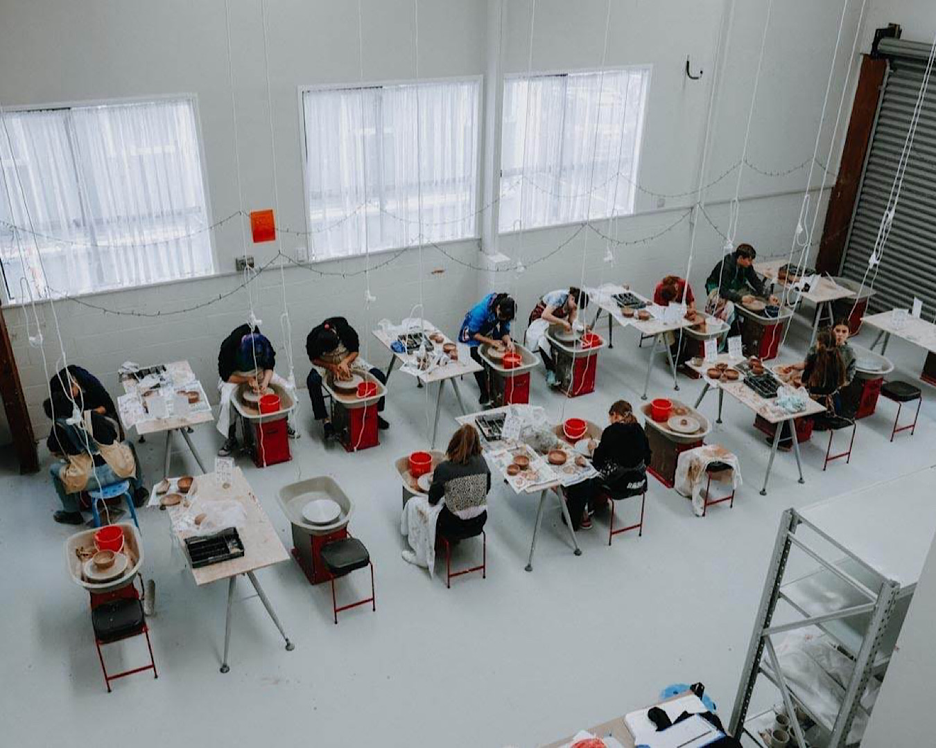 Birds eye view of people toiling away over individual pottery wheels at a workshop by The Clay Centre. 