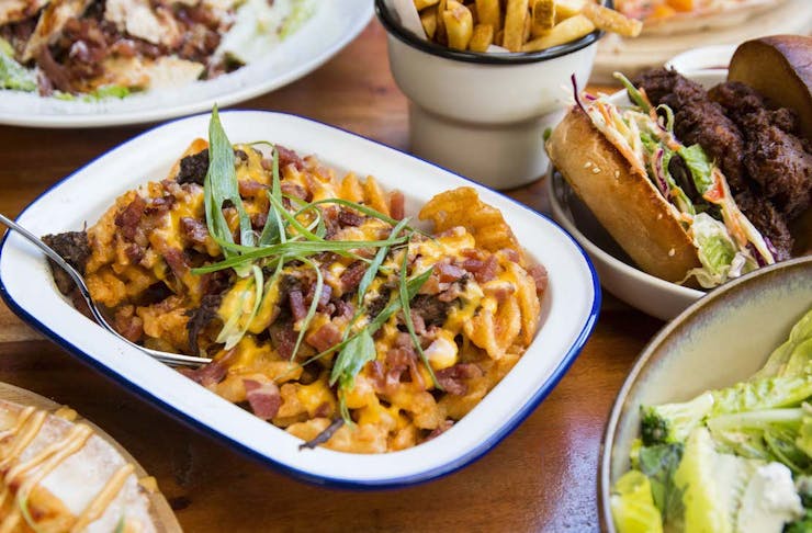 A spread of food, the main focus is a bowl of waffle fries topped with beef brisket