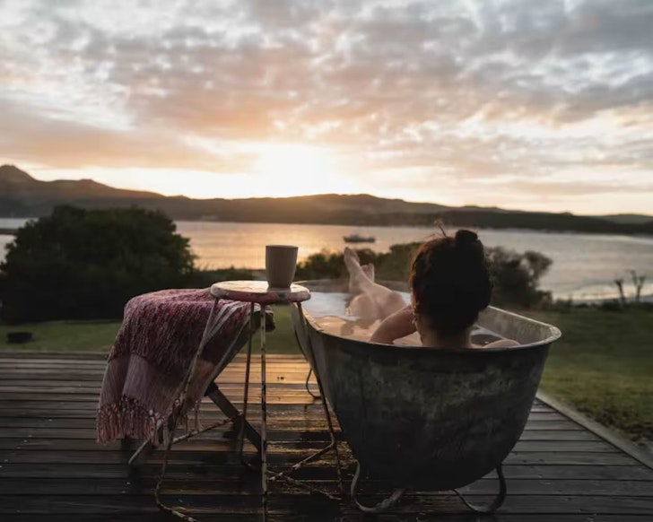 A woman lies in an outdoor bath at The Crayshack lake house Airbnb one of the best in Tasmania