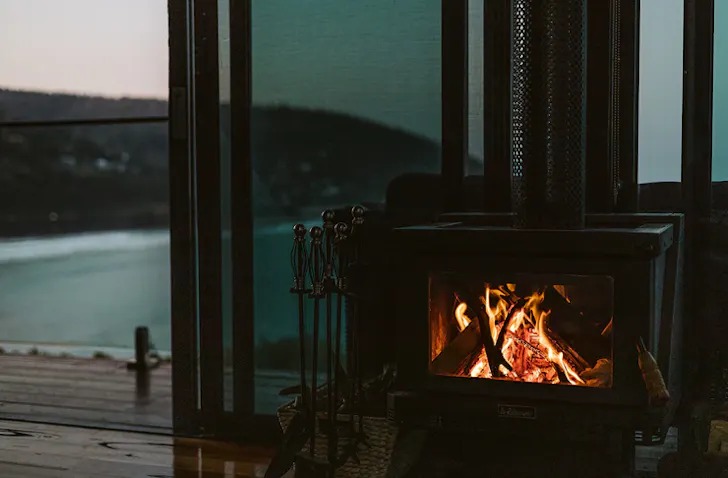 A fireplace is lit, sitting inside an Airbnb with the door leading to outside open behind it. 