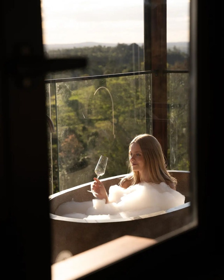 A woman sips champagne in an outdoor bath at The Firebreak in the Sunshine Coast