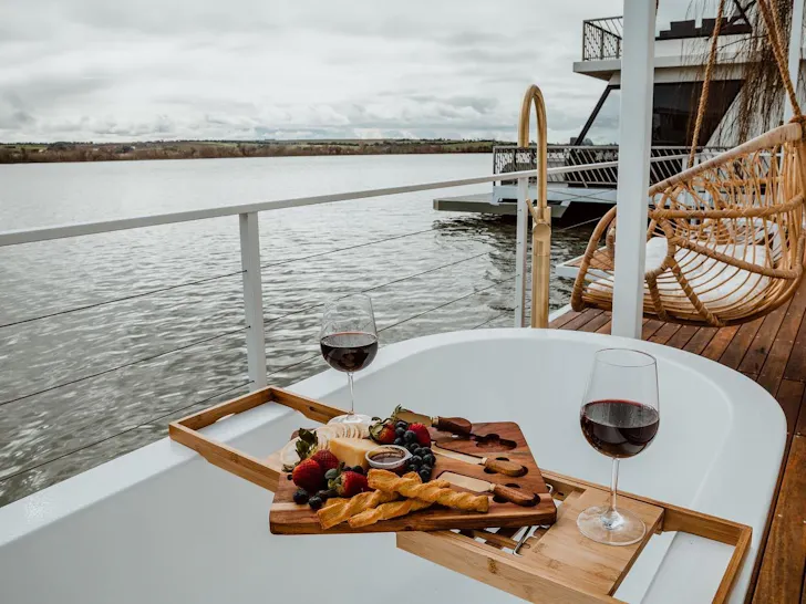 An outdoor bath, set with a cheesboard and glasses on red wine, sit on the deck of a floating home.