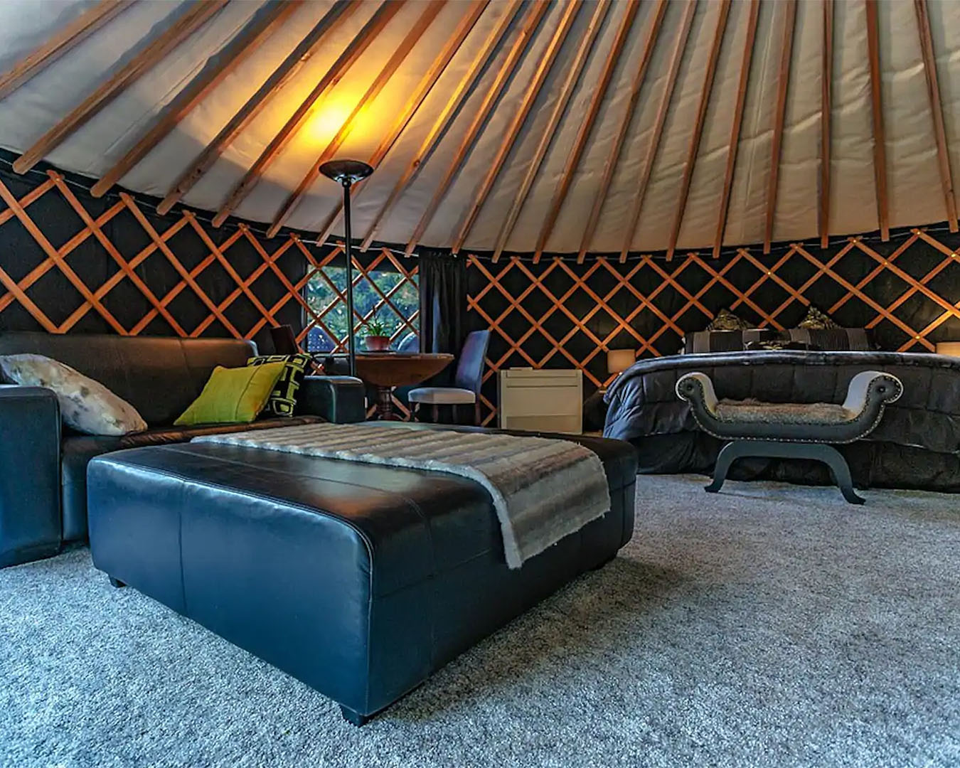 A Mongolian yurt in Bay of Plenty is seen from inside with comfortable leather sofa and bed in the distance. One of the best romantic getaways in Auckland.