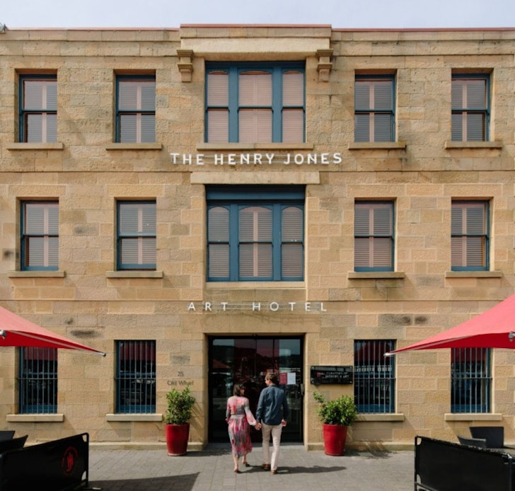 A couple walks into the Henry Jones Art Hotel one of the best hotels in Tasmania with red umbrellas either side