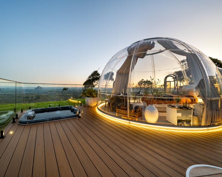 Mountaintop dome accomodation with deck and spa bath overlooking sunset view of mountains and the Sunshine Coast in the distance
