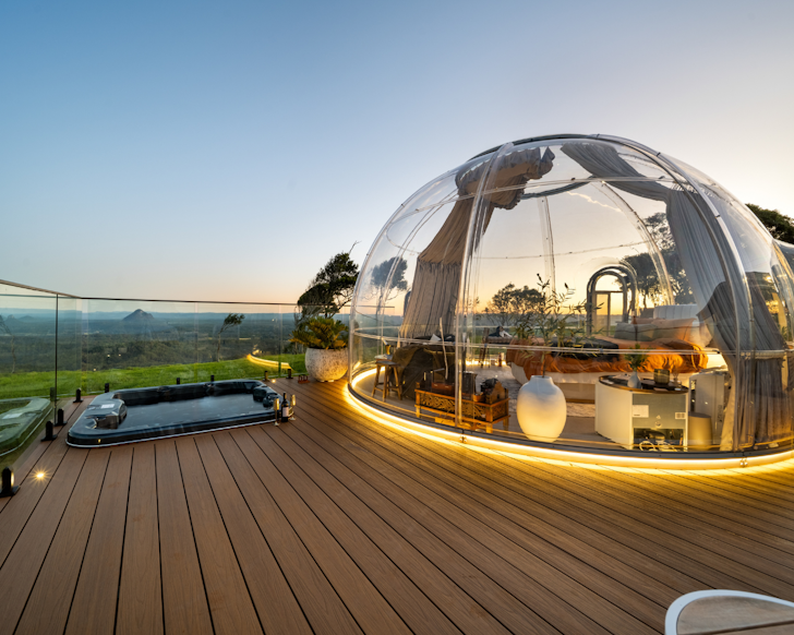 Mountaintop dome accomodation with deck and spa bath overlooking sunset view of mountains and the Sunshine Coast in the distance
