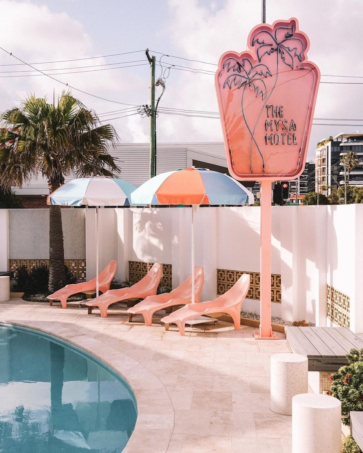 A view of the pastel pink motel sign at the Mysa Motel and sunloungers by the pool. It's one of the best motels in Australia