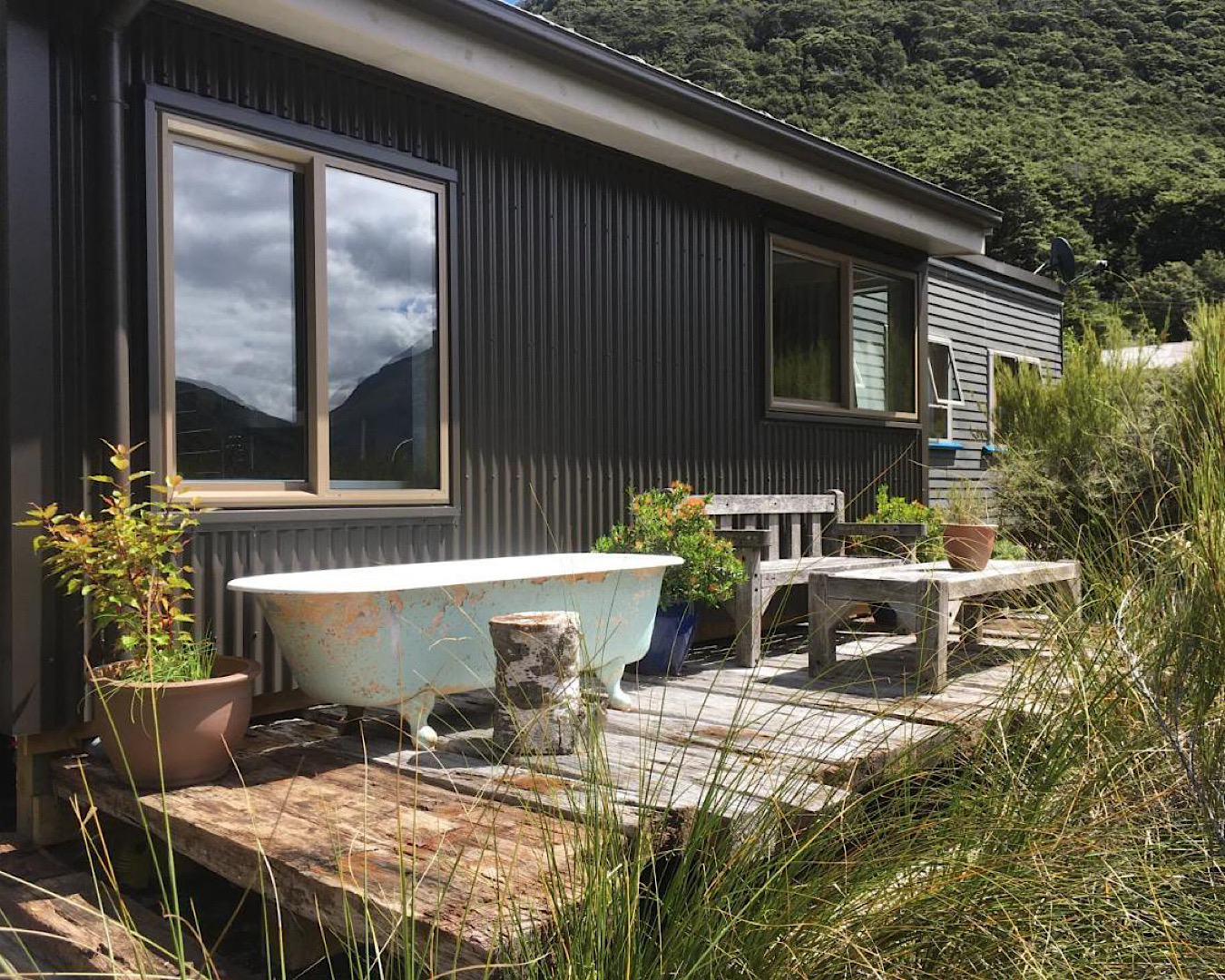 An outdoor bath with peeling paint sits on a modest deck on the side of a corrugated cabin. 