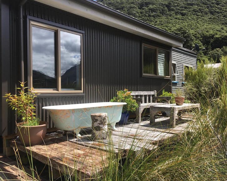 An outdoor bath with peeling paint sits on a modest deck on the side of a corrugated cabin. 