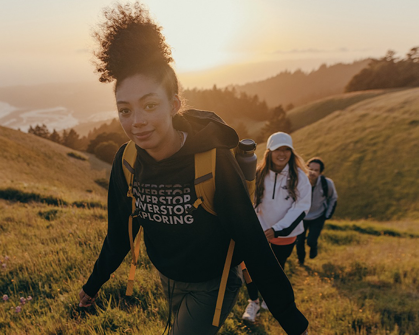 Three adventurous women wear The North Face activewear as they climb a hill, mid-tramp. 