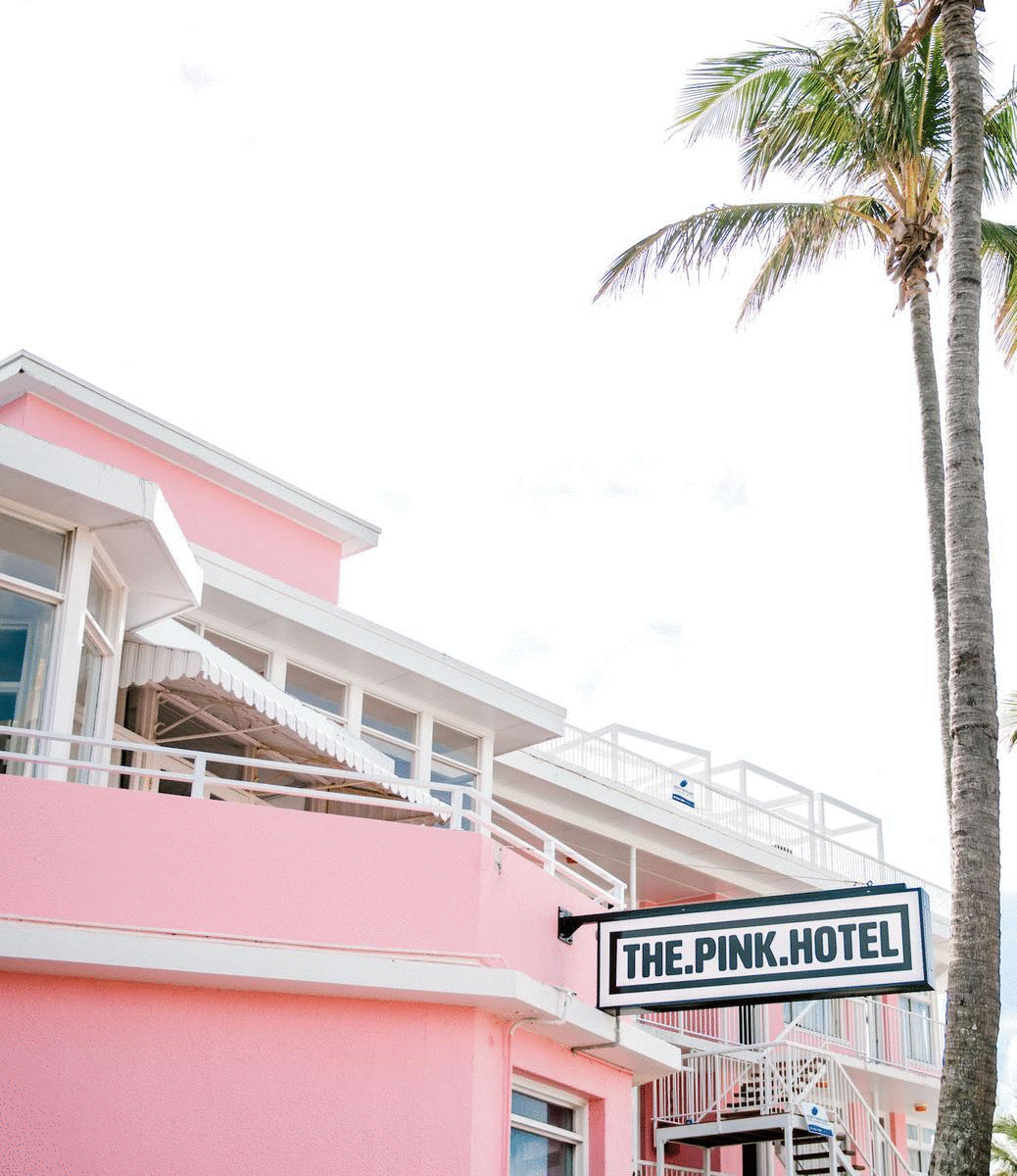 A vibrant pink hotel is surrounded by palm trees. 