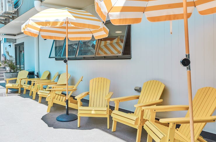 Bright yellow sun chairs sit underneath white and yellow striped umbrellas.