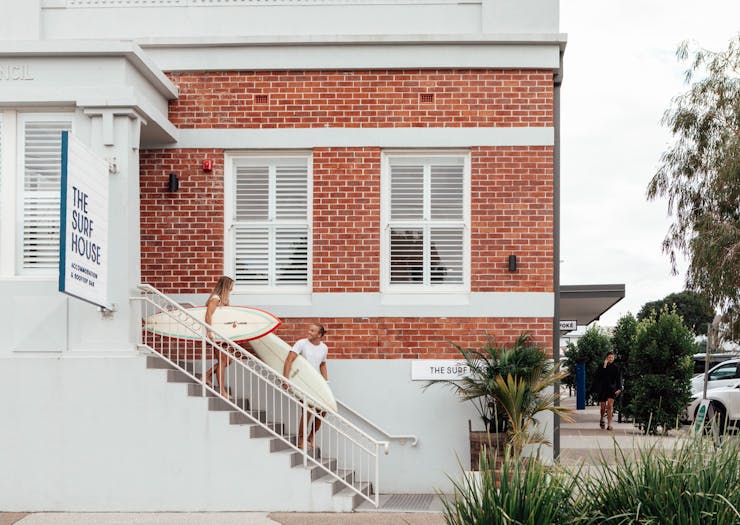 Two surfers walk down the stairs of The Surf House, a hostel in Byron Bay.