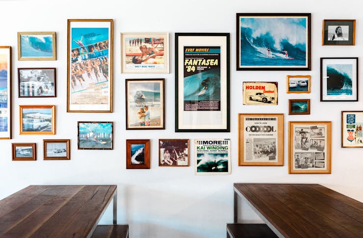 Two timber bar tables sit in front of a gallery wall featuring old surfing images.