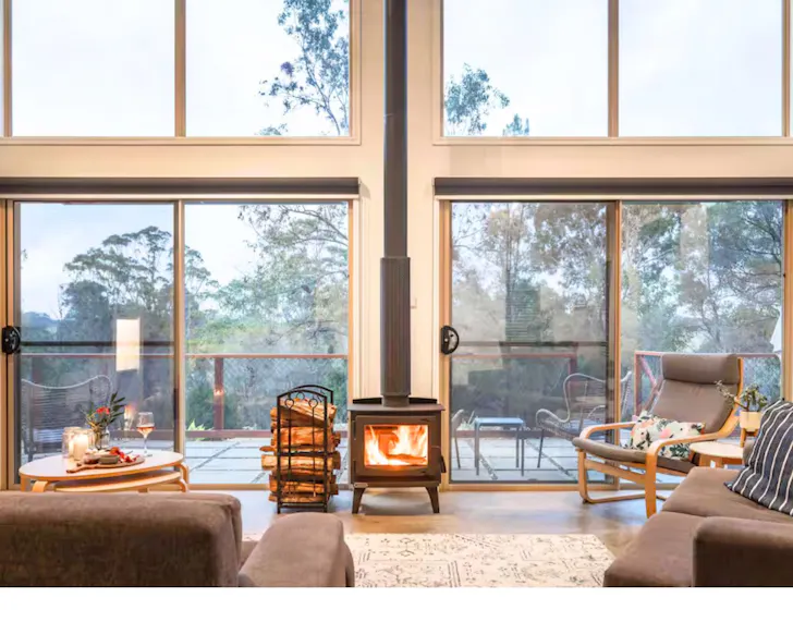 The indoor fireplace and huge windows of the living space at The Terrace Airbnb one of the best accommodation options near Narooma NSW