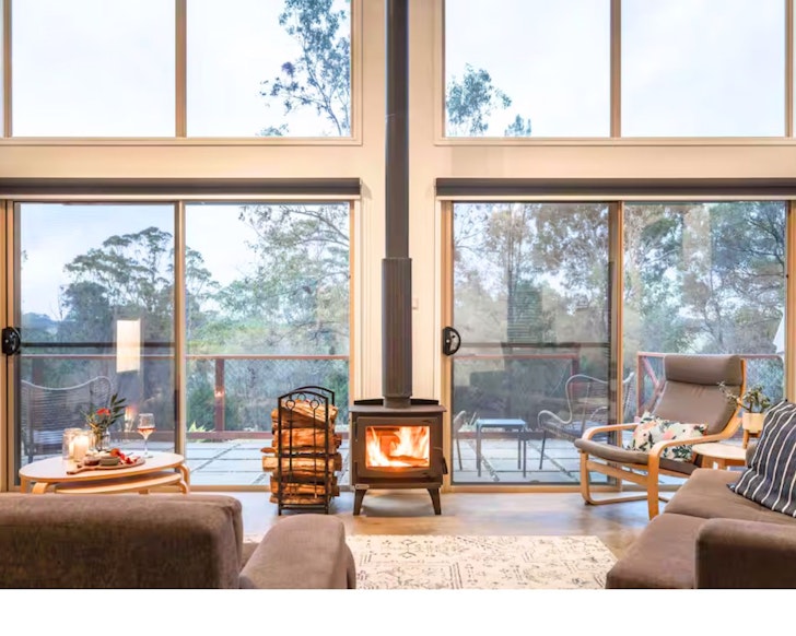 The indoor fireplace and huge windows of the living space at The Terrace Airbnb one of the best accommodation options near Narooma NSW