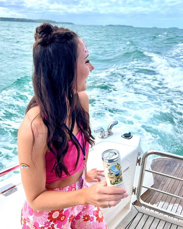 A girl dressed in pink festival attire stands on a boat holding a can of The Uncommon.