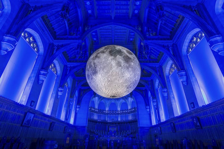 A moon lights up a building bathed in blue light.