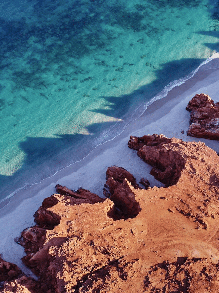 Blue ocean waters contrast with a vibrant orange dirt cliff. 