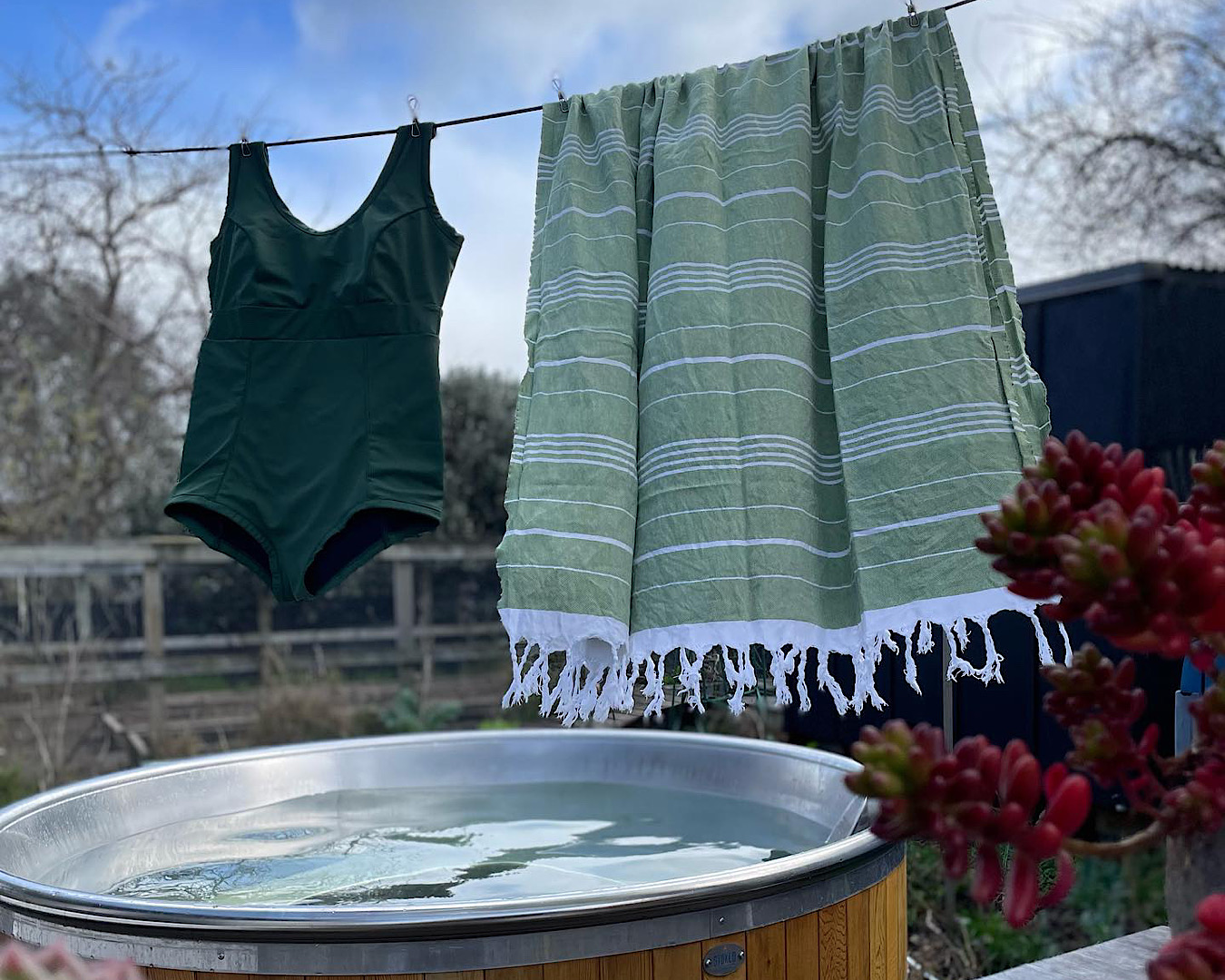A dark green retro-style swimsuit hangs on a washing line beside a light green Turkish towel. 