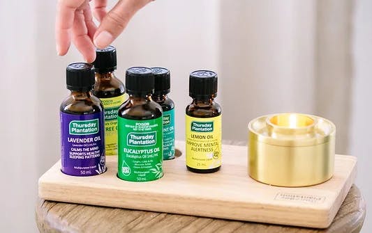 A hand reaching across four bottles of essential oils. 