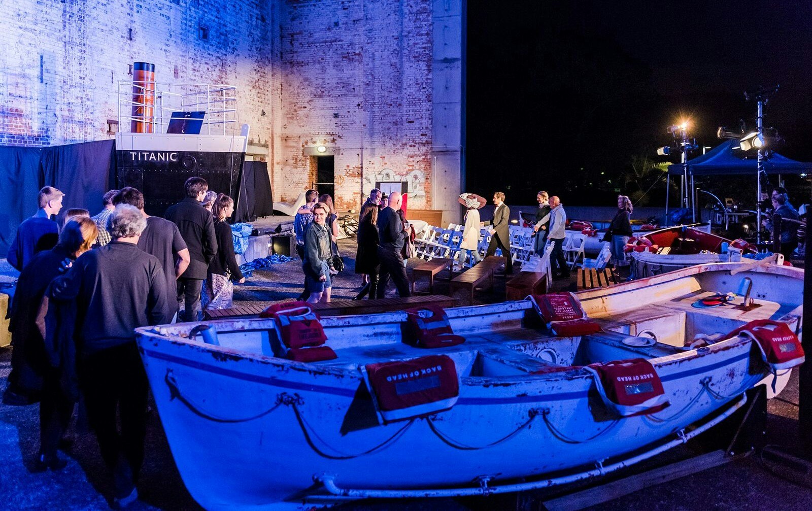 audience and cast standing near a life boat in a theatre