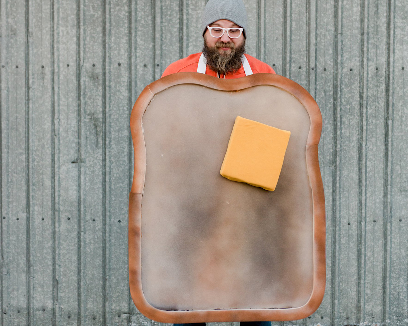 A man with a beard, glasses and a beanie wears a larger-than-life toast Halloween costume complete with a square of butter. 