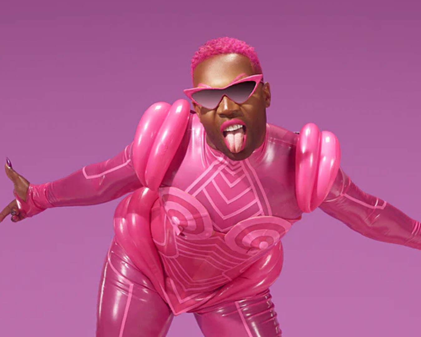 Toderick Hall leans into the camera bright pink semi-inflatable suit and long purple nails. 
