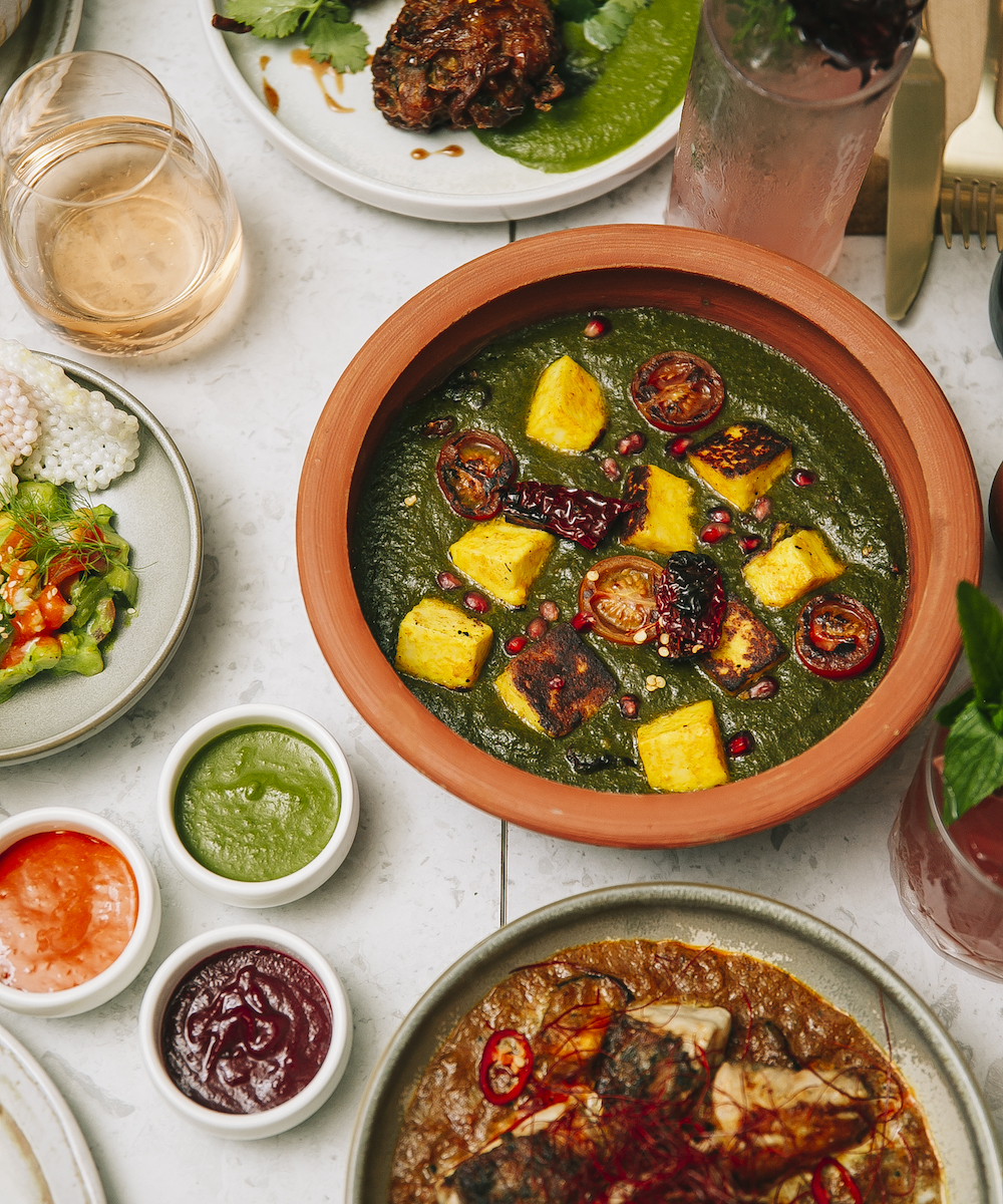a green-hued curry in a terracotta dish on a table surrounded by other yummy Indian share plates