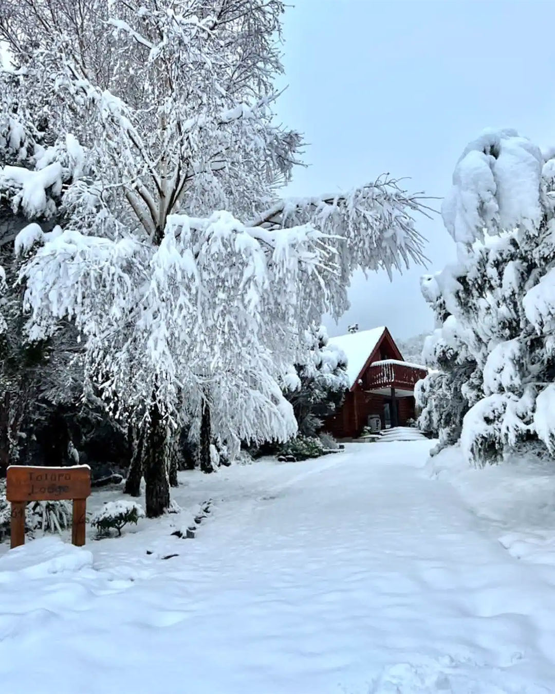 Totara Lodge is shown covered in snow from the outside with a sign pointing to it, one of the best airbnbs with fireplaces in NZ.