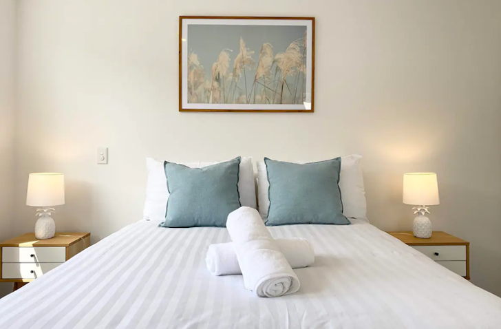 A nicely-dressed white bed with baby blue cushions at comfy townhouse, one of the best airbnbs in Christchurch