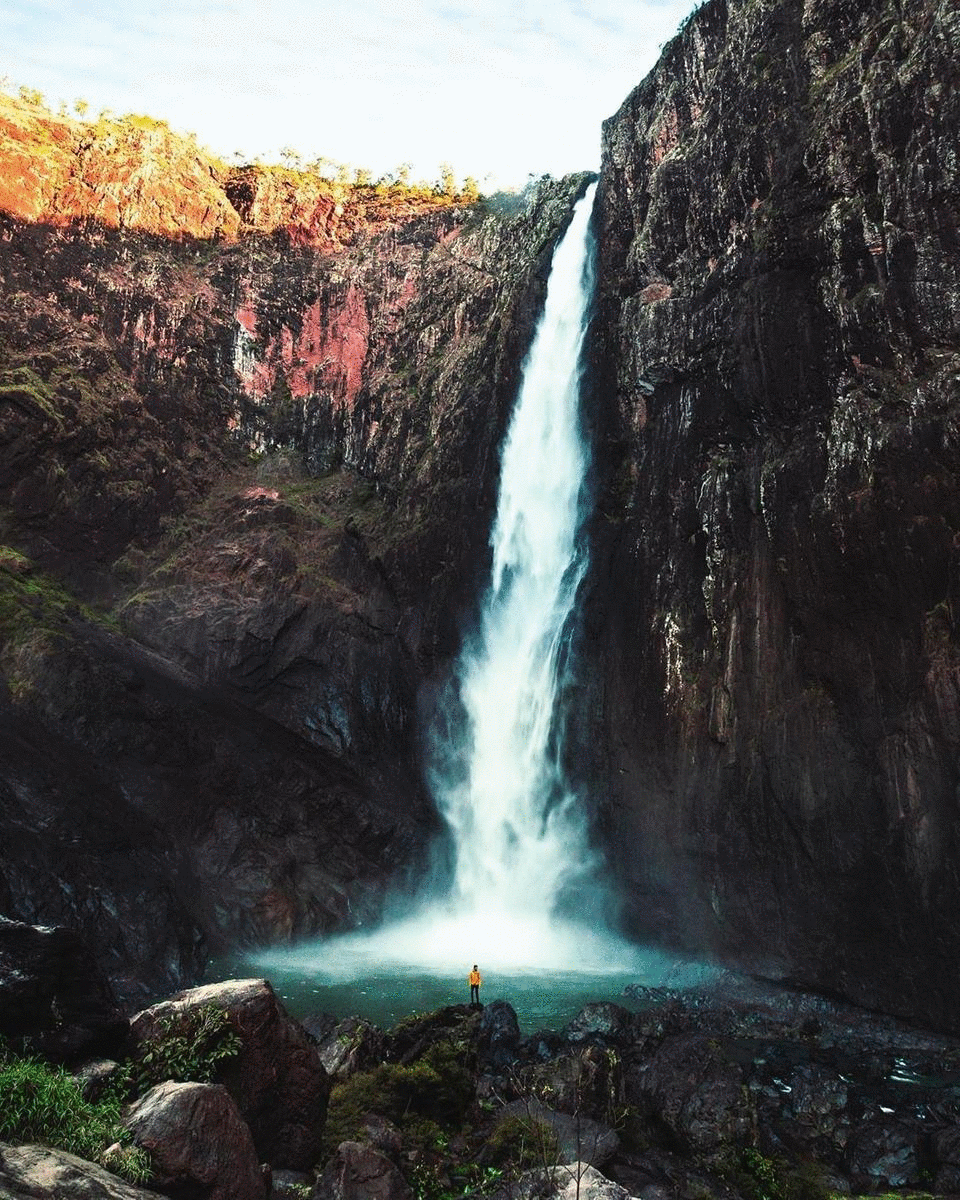 A man stands at the bottom of a cascading waterfall. 