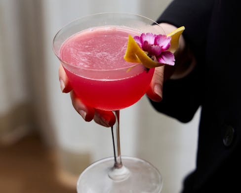 Holding a ruby red cocktail. 