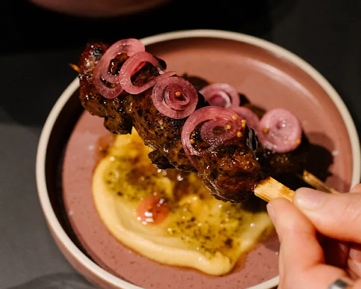 Vicki holds a skewer of meat, topped with pink onion rings. 