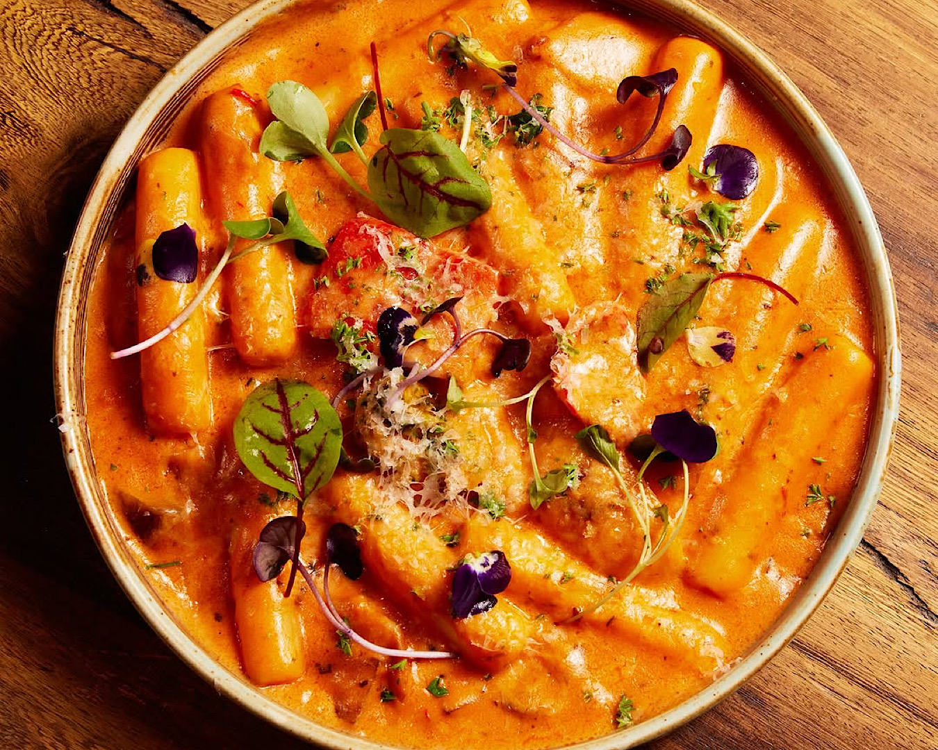 A bowl of creamy rose tteokbokki topped with parmesan and a smattering of glorious microgreens. 