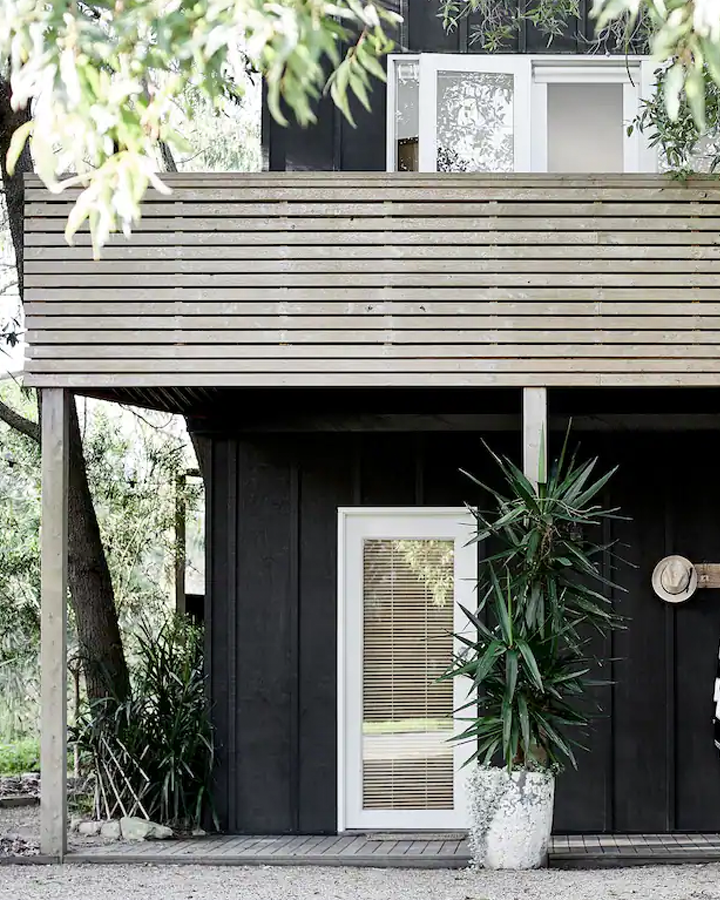 A large black and raw wooden beach shack with trees, a mornington peninsula accommodation.