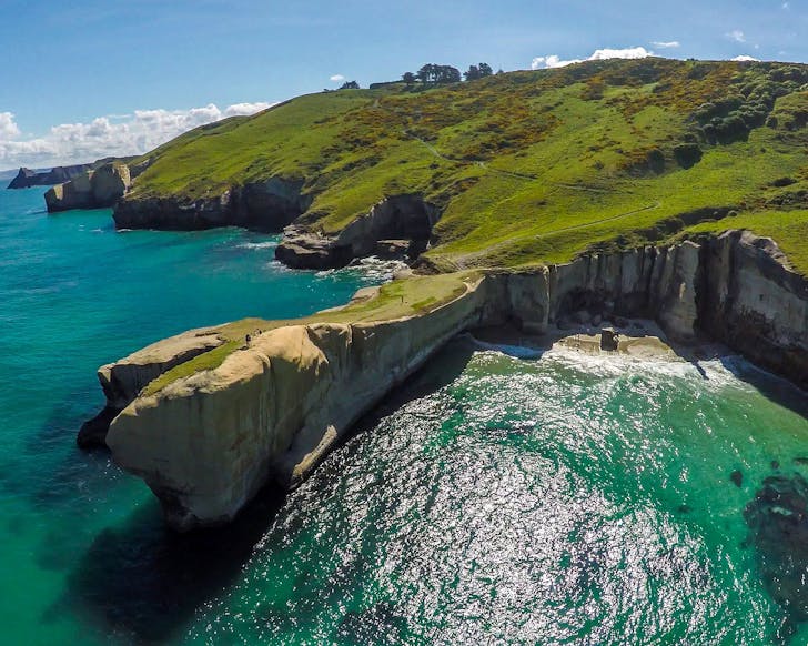 An aerial view of Tunnel Beach in Dunedin shows a stunning coastline and blue green water.