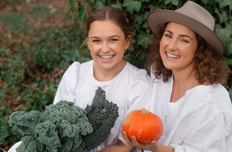 Rosa and Margo from Two Raw Sisters smile at the camera while holding fresh produce.