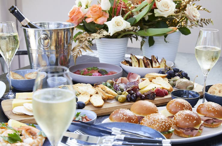 A spread of delicious food including sliders, an assortment of cheeses, fresh bread and champagne.