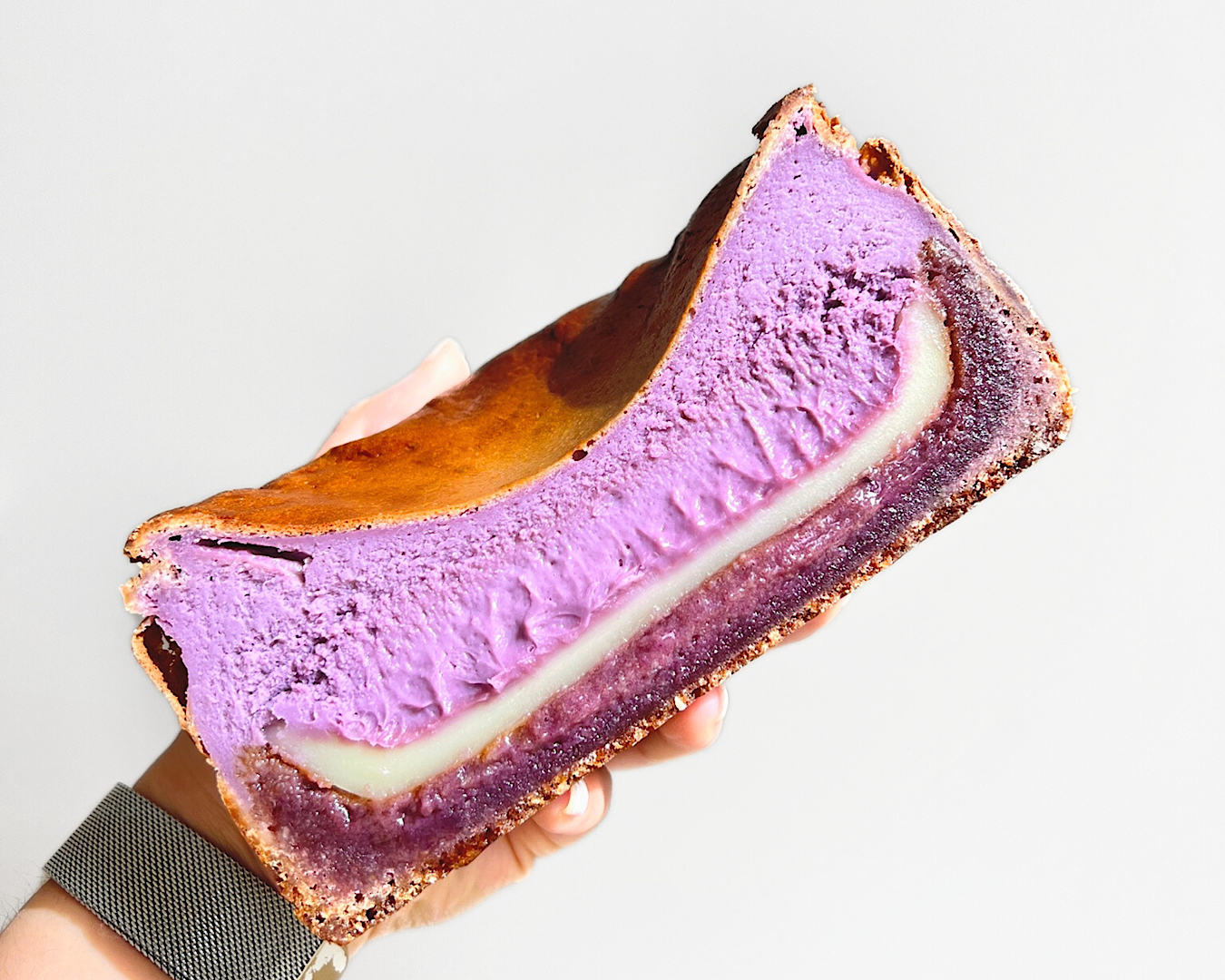 Someone holds half of a purple mochi-stuffed ube burnt Basque cheesecake. 