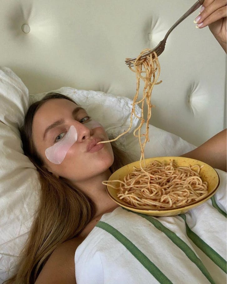 Lady laying bed who's eating her pasta
