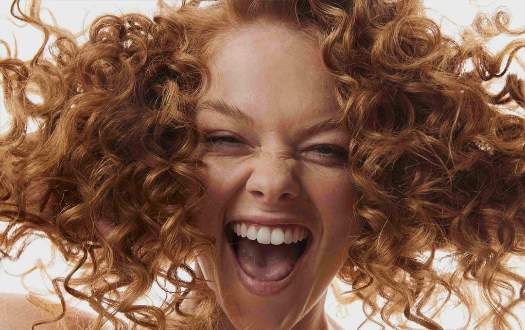 A person with curly hair smiling into a camera. 