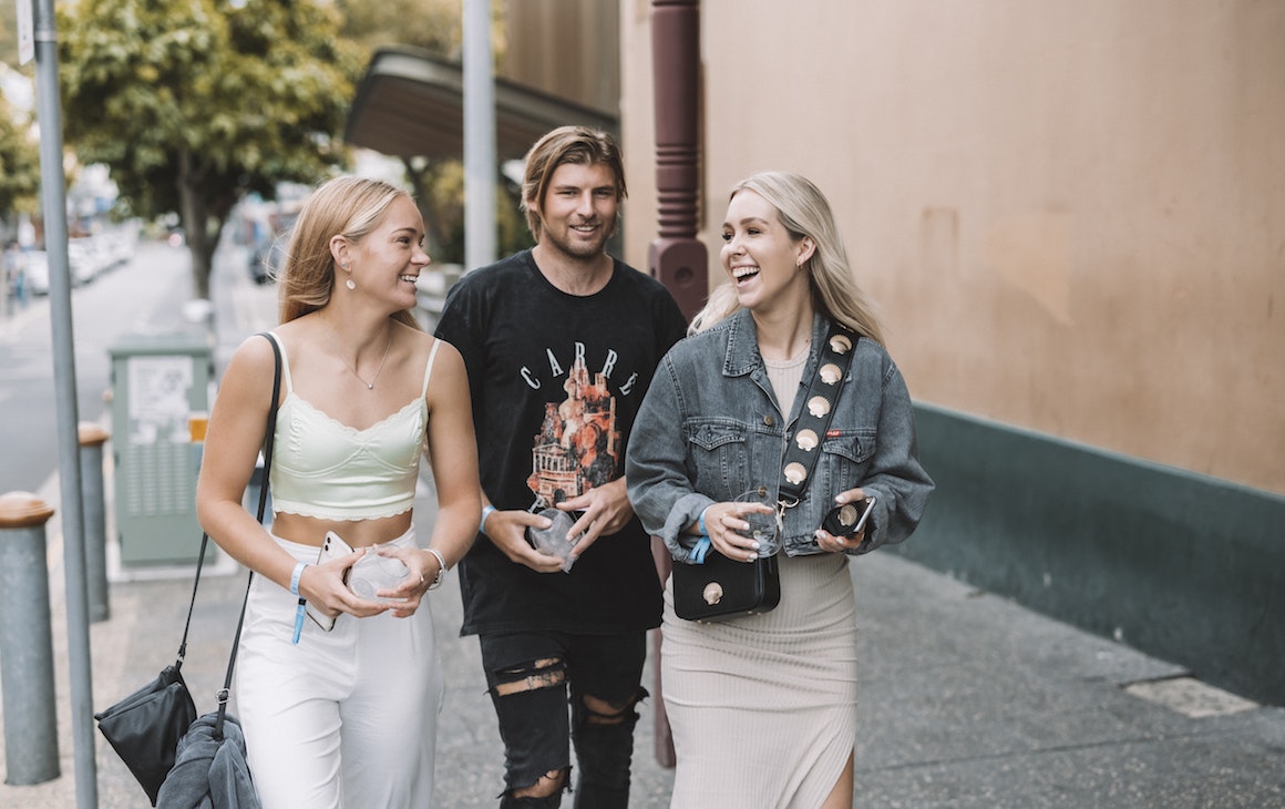 three people walking in the street golding wine glasses