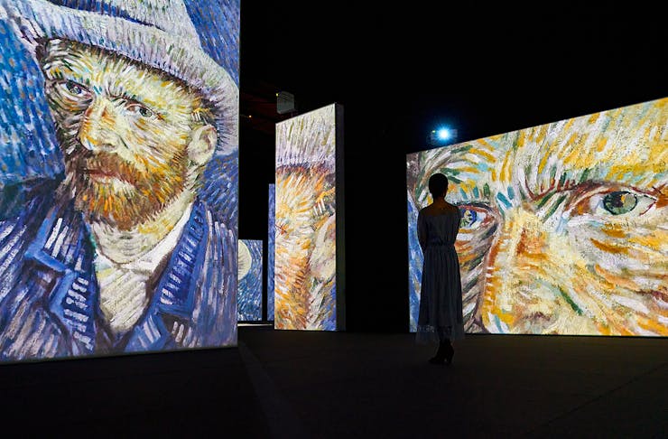 A person takes a picture of a huge Vincent Van Gogh self portrait projected onto a wall.