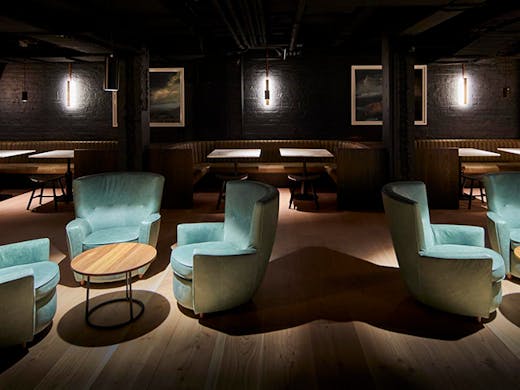 The dimly lit interior of Valhalla with suede cyan blue chairs and booth seating in the background 
