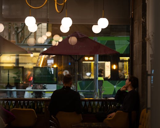 Two people sitting at a bar with lights above them. 