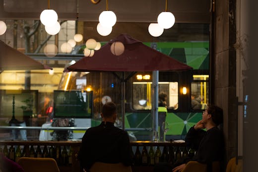 Two people sitting at a bar with lights above them.